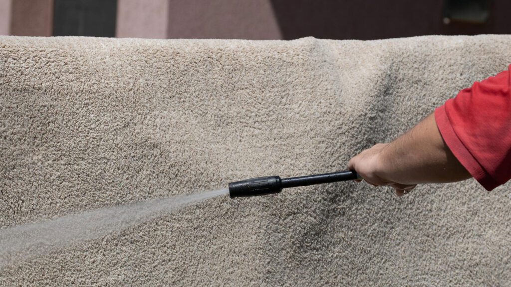 man washing carpet with water gun